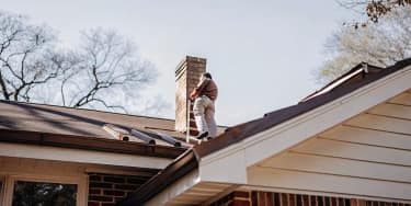 Professional roofer inspecting metal roof flashing on a residential Texas home with chimney