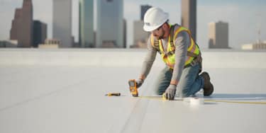 Roofing professional inspecting a white TPO membrane on a commercial building in Texas